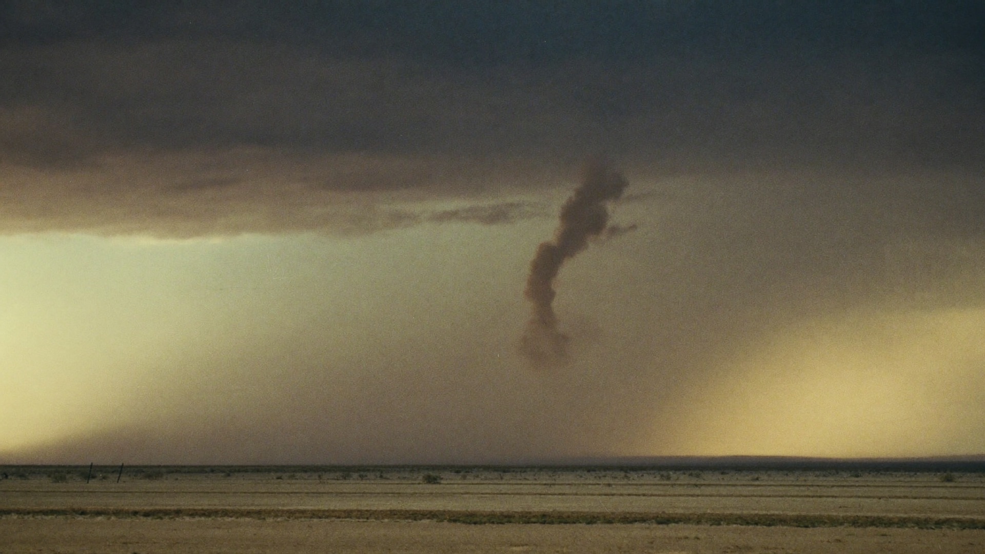 A lone monsoon storm cell over open desert flats, a rain curtain falling in the distance